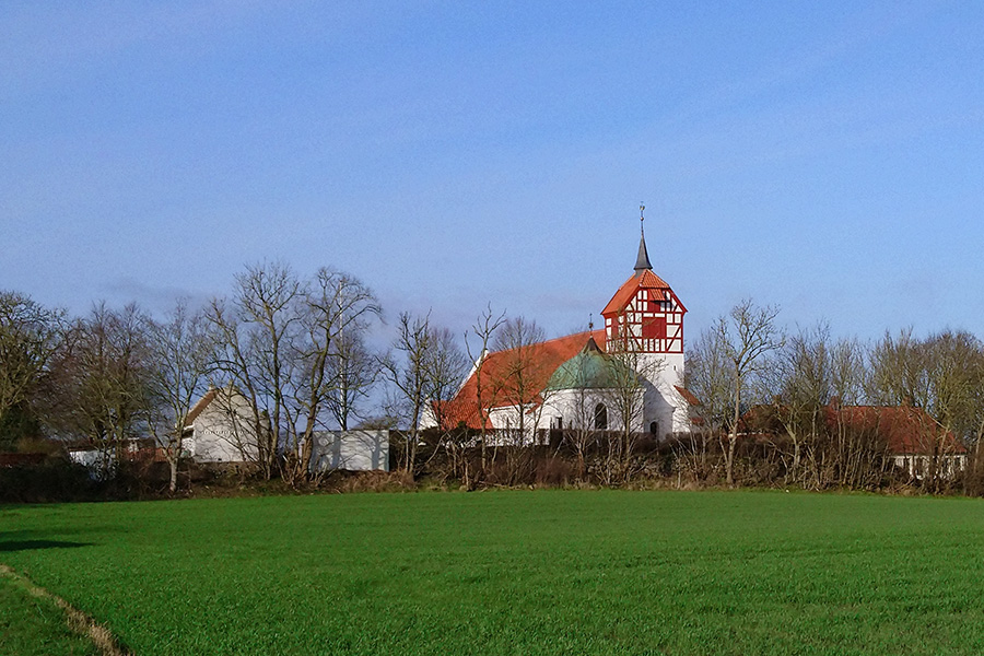 Viby Kirke set fra sydøst med blå himmel som baggrund og med grøn mark i forgrunden. Hvidkalkede vægge og nyt, rødt tegltag på skib og tårn.