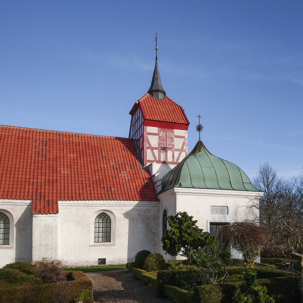 Østlig halvdel af Viby Kirke set fra syd fra kirkegården med gravsten og beplantning i forgrunden og blå himmel i baggrunden. Hvidkalkede vægge og nyt, rødt tegltag på skib og tårn.